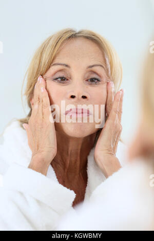 Donna anziana l'applicazione di crema per il viso sulla sua pelle Foto Stock