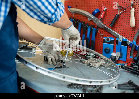 Maschio in mani guanti tessili del bullone di fissaggio sulla parte centrale della ruota di bicicletta Foto Stock