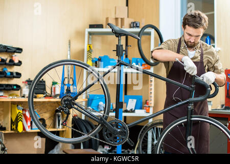 Uomo in grembiule e guanti il fissaggio manubrio di bicicletta in officina Foto Stock