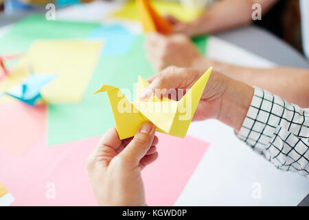 Le mani umane ripiegare il foglio di carta gialla mentre rendendo uccello origami Foto Stock