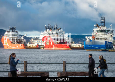 Bergen, Norvegia - Ottobre 2017 : la gente che camminava su un lungomare con grandi navi da carico nel porto di Bergen in background, Norvegia Foto Stock