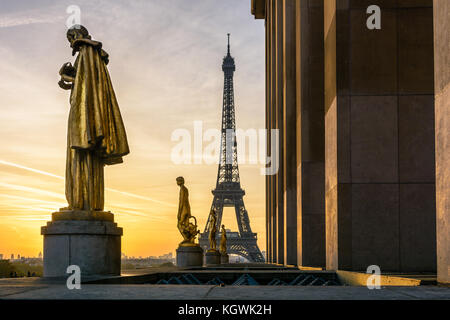 Il sole illumina il golden statue del Trocadero mentre la Torre Eiffel si staglia contro un cielo arancione. Foto Stock