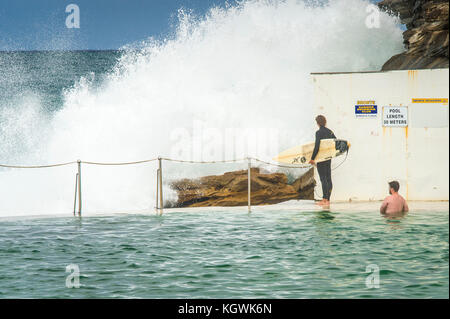 Un surfista maschio attende il momento giusto per entrare in acqua da Bronte Beach rock pool di Sydney, NSW, Australia in grandi condizioni surf Foto Stock