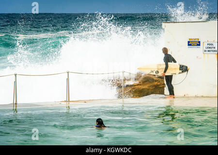 Un surfista maschio attende il momento giusto per entrare in acqua da Bronte Beach rock pool di Sydney, NSW, Australia in grandi condizioni surf Foto Stock