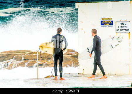 Due surfisti attendere il momento giusto per entrare in acqua da Bronte Beach rock pool di Sydney, NSW, Australia in grandi condizioni surf Foto Stock