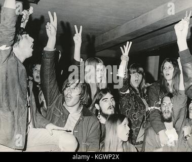 Un grande gruppo di studenti che indossano abiti hippie, tra cui abbigliamento psichedelico a motivi geometrici, bracciali anti-guerra e capelli lunghi, tengono le dita in alto in un gesto di pace durante un sit-in di protesta contro gli studenti della North Carolina State University di Raleigh, North Carolina, con alcuni studenti che tengono in alto fiori di pace e indossano fiori nelle loro fasce, 1970. () Foto Stock