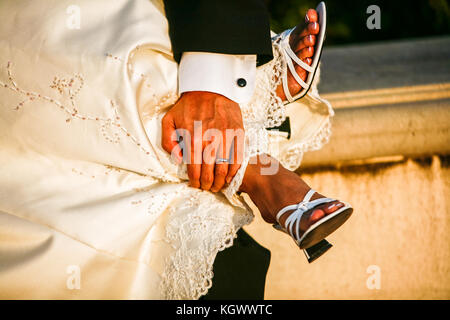 Vista ravvicinata di un groom la mano sulla sposa i piedi nella calda luce del tramonto Foto Stock