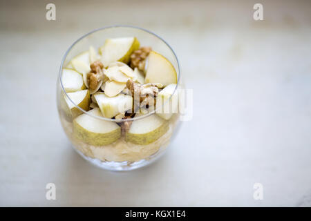 Farina di avena crema di farina e di latte aromatizzato con purea di banana, guarnita con fette di pera, noci, mandorle e miele, vista da sopra, servita in un chiaro vetro rotondo, pla Foto Stock