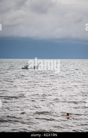 Sarbinowo, Polonia - Agosto 2017 : uomo nuotare lontano dalla riva con la burrascosa cieli sopra e fisherman barca a distanza Foto Stock