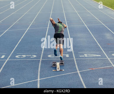 Vista posteriore di un atleta di iniziare il suo sprint su un all-weather via di corsa. Runner con blocco di partenza per iniziare la sua esecuzione sulla pista. Foto Stock