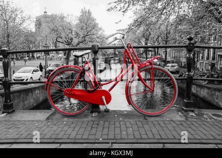 Una foto di un solitario red bici sul ponte sul canale di Amsterdam. Lo sfondo è bianco e nero. Foto Stock