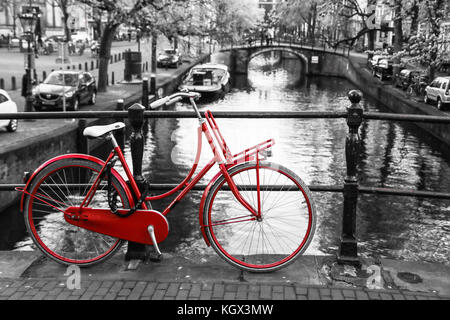 Una foto di un solitario red bici sul ponte sul canale di Amsterdam. Lo sfondo è bianco e nero. Foto Stock