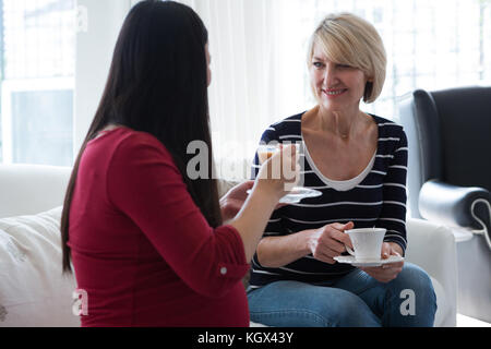 Amici di sesso femminile che interagiscono con ogni altro pur avendo il tè nel soggiorno Foto Stock