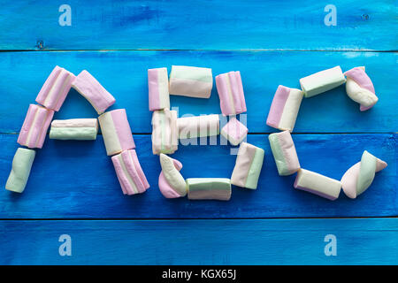 Abc lettere fatte di caramelle marshmallow, vista da sopra, isolata, blu sullo sfondo di legno Foto Stock