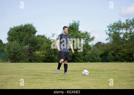 Giocatore di calcio che giocano a calcio nel terreno in una giornata di sole Foto Stock