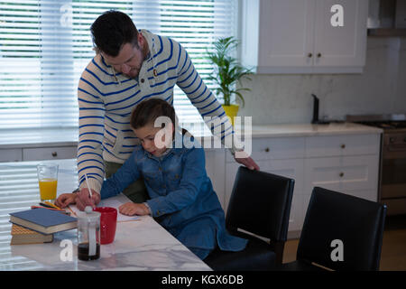 Padre ad assistere la figlia in i suoi studi a tavola Foto Stock