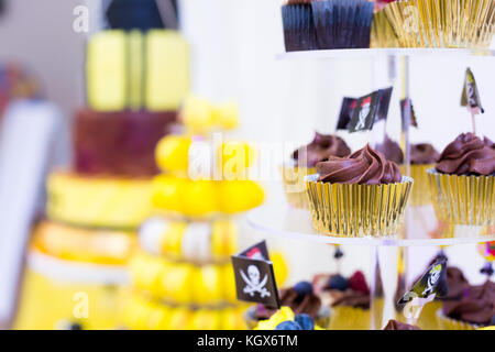 Ragazzo festa di compleanno torte con focus sui tortini di cioccolato con bandiere pirata, posto su un piedistallo di torta. torte dolci sul tavolo, giallo e nero PAL a colori Foto Stock