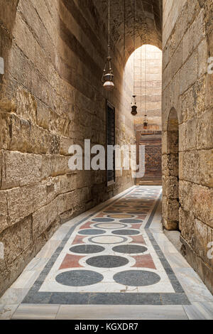 Corridoio ad arco che conduce al cortile del sultano barquq moschea con mattoni di pietra a parete, ornata di marmi colorati pavimenti e porte in legno, vecchio cairo, Egitto Foto Stock