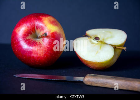 Tutto rosso, mature, gustoso apple con un coltello, metà di Apple e su sfondo nero Foto Stock