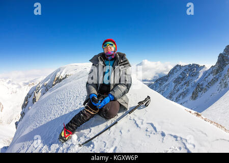 Donna scalatore in casco e down jacket con bastoncini da trekking si trova sulla cima di una montagna. Foto Stock