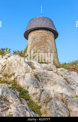 Cerca fino a melin wynt y craig windmill seduto su uno sperone roccioso a Llangefni, Anglesey, un mulino a vento convertito, ora un telefono cellulare torre di comunicazione Foto Stock