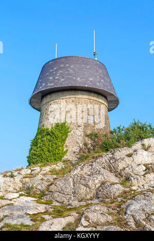 Cerca fino a melin wynt y craig windmill seduto su uno sperone roccioso a Llangefni, Anglesey, un mulino a vento convertito, ora un telefono cellulare torre di comunicazione Foto Stock