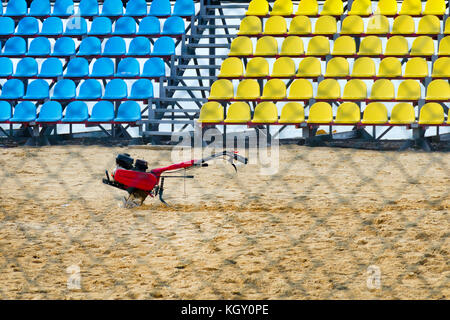 Coltivatore sorge sulla spiaggia nel centro di un piccolo sportivo stadio con il blu e il giallo sedi dei tifosi. Foto Stock