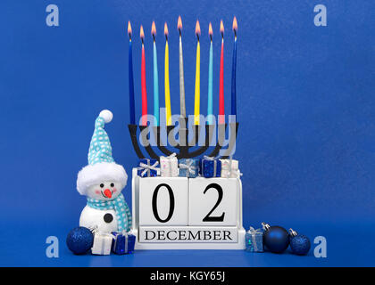 Calendario in legno raffigurante i blocchi data per hanukkah 2018, dicembre 02 con menorah bruciando dietro showman indossando blu, piccoli regali su blu testurizzato Foto Stock