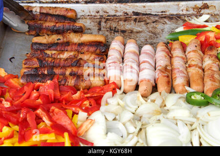 Pancetta avvolto hot dogs, cipolle, jalapenos, e diverse varietà di peperoni grigliare su un fornitori esterni grill. close up. Foto Stock