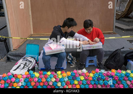 Un americano cinese giovane fa coloratissimi fiori origami e incarica il suo amico a fare lo stesso. A Union Square Park di New York City. Foto Stock