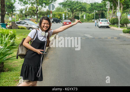 Donna sorridente in attesa e salutando taxi Foto Stock