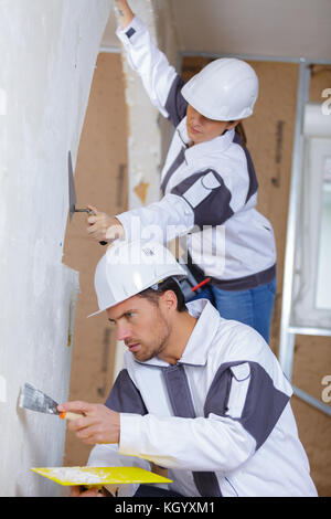 Due costruttori in hardhats e tuta con la spatola la riparazione di camera Foto Stock