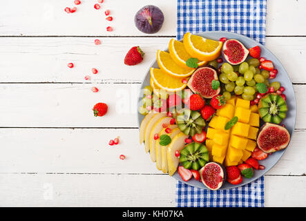 Piatto di frutta e bacche. mango, kiwi, fichi, fragole, uva, pera e arancia. cucina vegana. menu dietetici. flat laici. vista superiore Foto Stock