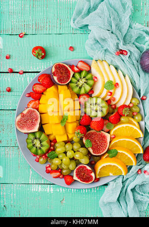 Piatto di frutta e bacche. mango, kiwi, fichi, fragole, uva, pera e arancia. cucina vegana. menu dietetici. flat laici. vista superiore Foto Stock