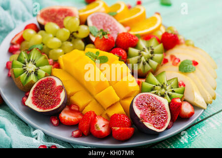 Piatto di frutta e bacche. mango, kiwi, fichi, fragole, uva, pera e arancia. cucina vegana. menu dietetici. Foto Stock