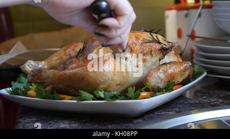 Mani femminili decorano arrostito intero pollo sulla piastra per la cena in famiglia. Foto Stock