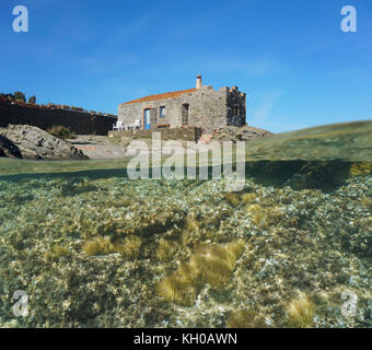 Al di sopra e al di sotto della superficie dell'acqua, vecchia casa lapideo in riva al mare con gli anemoni di mare e alghe sottomarine, mare mediterraneo, cadaques, Costa Brava, SPAGNA Foto Stock