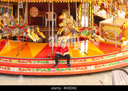 Un lavoratore della fiera guarda al telefono seduto su un merry-go-round sul lungomare di Brighton Foto Stock