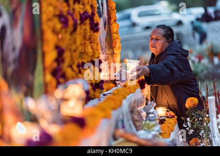 La madre di due fratelli uccisi lo stesso giorno accende candele sulla loro tomba decorata durante il giorno del festival dei morti 31 ottobre 2017 a Tzintzuntzan, Michoacan, Messico. Foto Stock