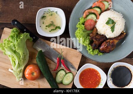 Preparazione del popolare piatto malese nasi ayam o pollo con riso cotto pollo a pezzi, pomodoro, cetriolo, insalata, zuppa, la salsa di soia e salsa di peperoncino. Foto Stock