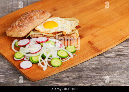 Sandwich con pancetta e uova di pollo con radicchio e cipolla cetrioli con uova fritte e pancetta, deliziosa prima colazione Foto Stock