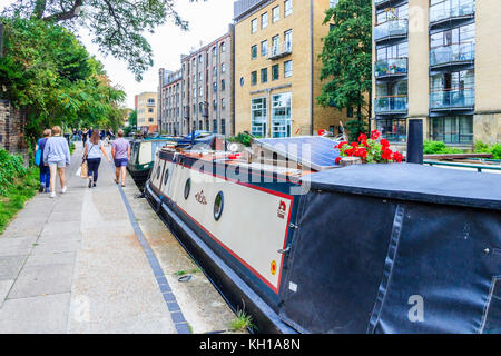 La gente a piedi sulla strada alzaia del Regent's Canal passato narrowboats ormeggiato a Battlebridge bacino, King's Cross, London, Regno Unito Foto Stock