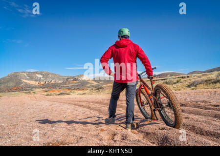 Un maschio stanco ciclista con un grasso bike contemplando una dura e lunga corsa attraverso la ghiaia profonda sul foro grande Lavare Trail in Montagna Rossa spazio aperto, colora Foto Stock