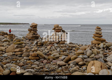 Un uomo cammina la spiaggia fiancheggiato da uomo fatto di pile di pietra / cairns sulla Isola Santa Foto Stock