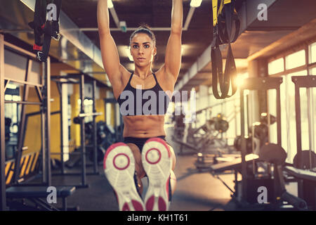 Ragazza sulla formazione in palestra tira bar ed esercizi six pack Foto Stock