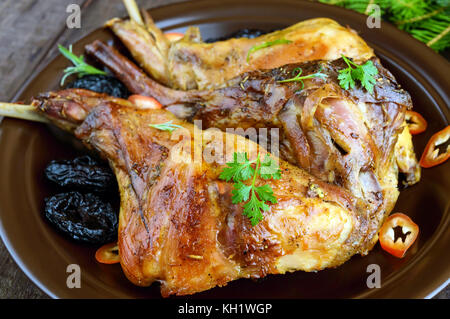 Arrosto di coscia di coniglio con prugne su una piastra di ceramica su legno scuro dello sfondo. close up. vacanze menu. Pasqua e Natale. Foto Stock