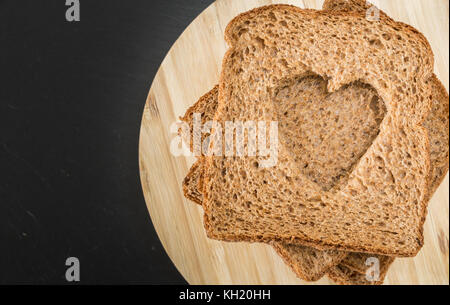 Grano intero sandwich fette di pane con cuore forma di taglio, sul piatto di legno Foto Stock