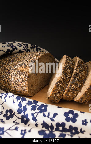 Tutto il grano pane affettato closeup , su una superficie di legno con motivi floreali asciugamano da cucina. Foto Stock