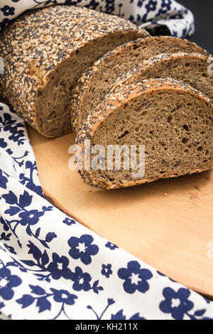 Tutto il grano pane affettato closeup , su una superficie di legno con motivi floreali asciugamano da cucina. Foto Stock