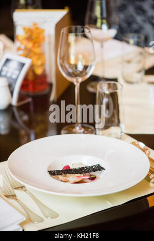 Un piatto di pesce disposto su un tavolo da pranzo con un'acqua vuota e un bicchiere di vino dietro di esso Foto Stock